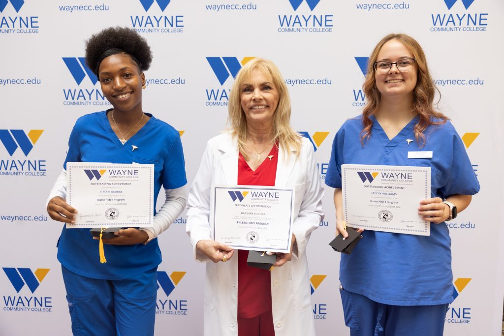 Three individuals stand together holding certificates.