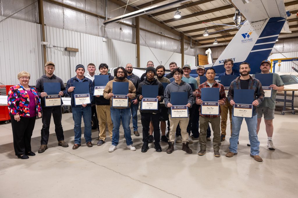 Individuals stand in front of an airplane holding certificates.