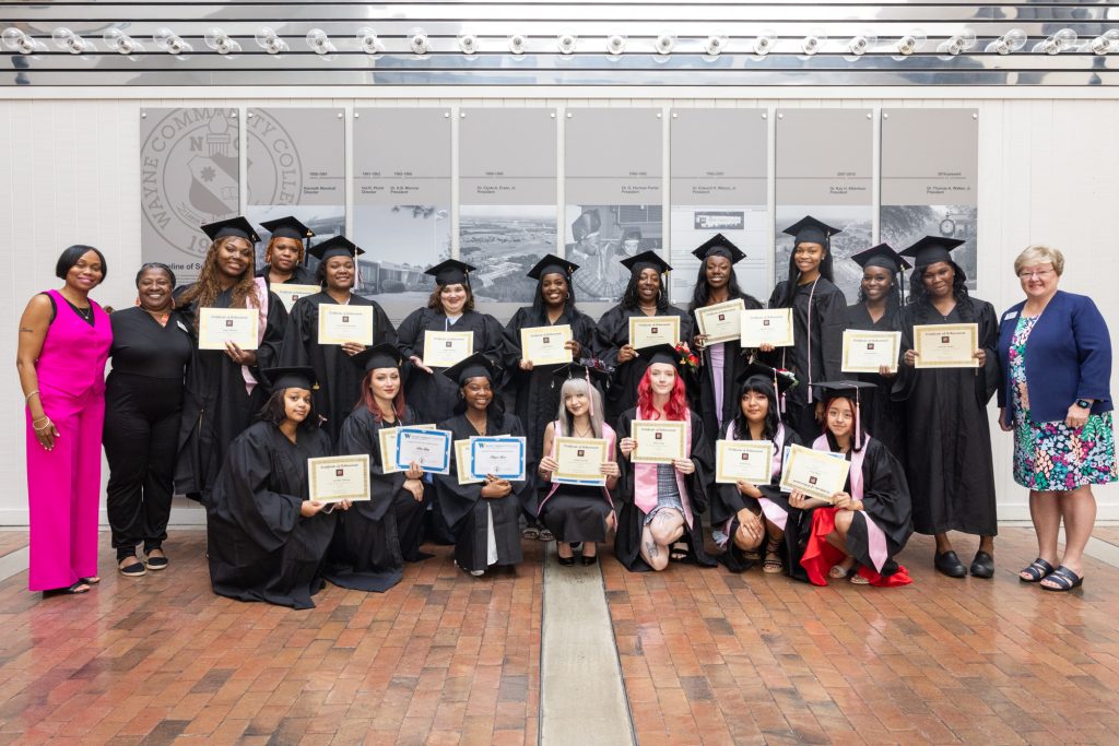 Students stand together holding certificates while wearing graduation caps and gowns.