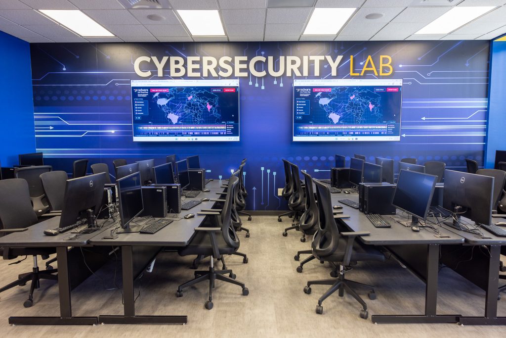 Computer monitors on tables in front of a wall displaying screens.