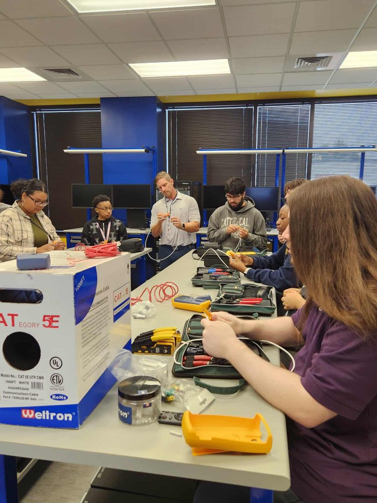 Individuals sit and stand around a table working with cables.