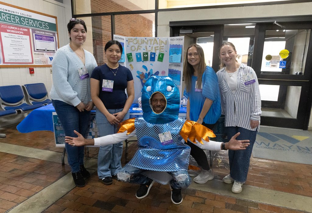 A group of people stand around a poster with one person wearing a costume.