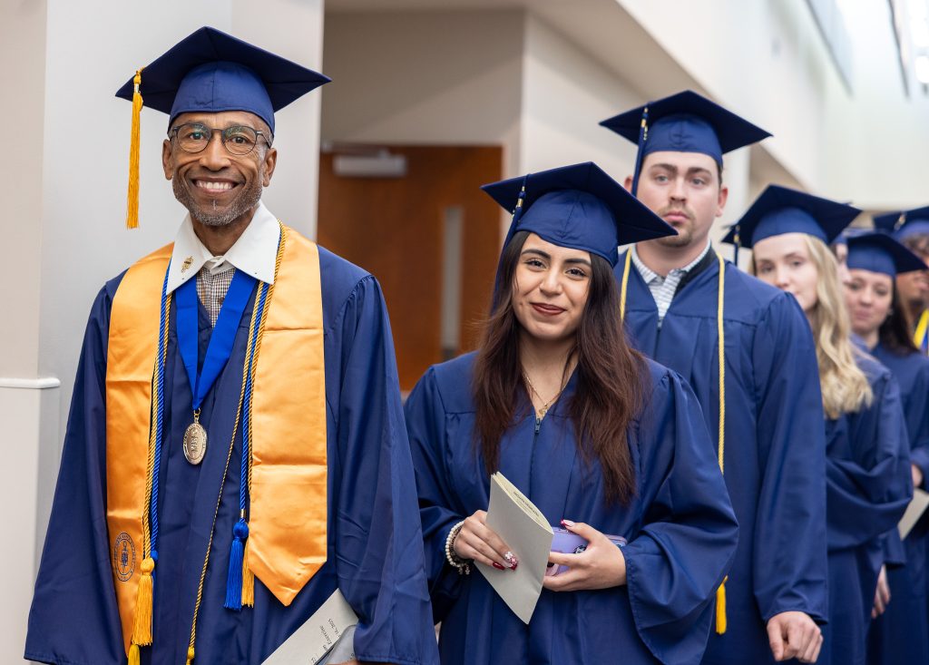 Individuals stand together wearing graduation caps and gowns.