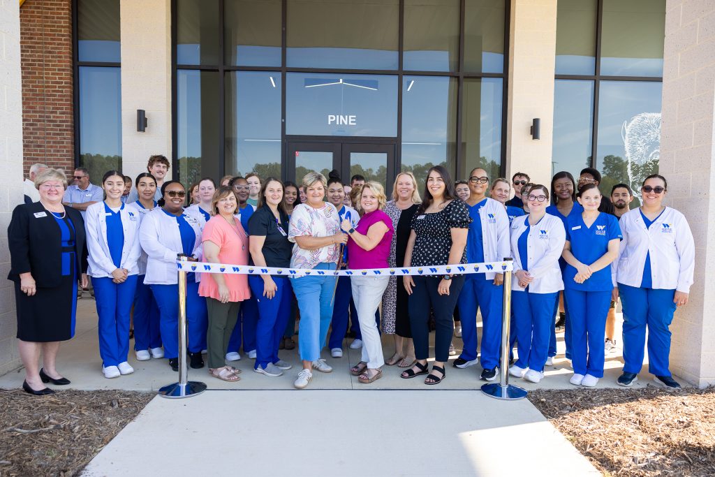 Individuals stand in front of a ribbon outside of a building.