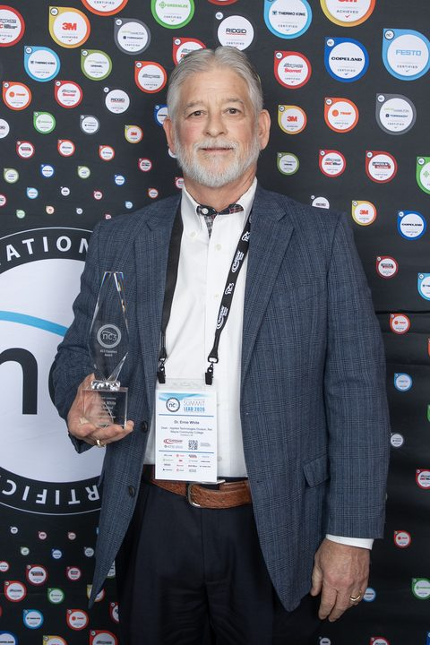 A man stands in front of a backdrop while holding an award plaque.